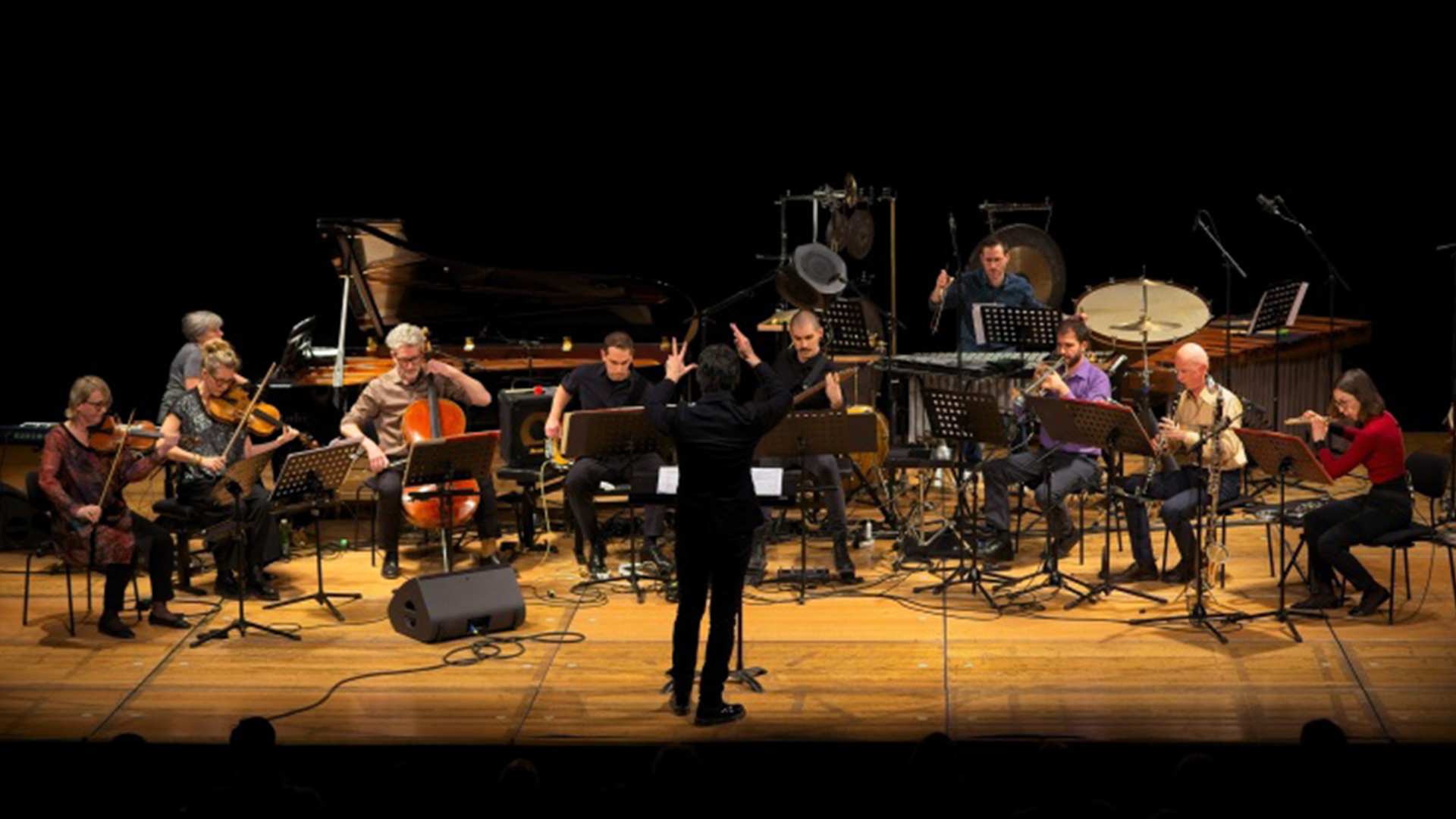 Foto von spielendem Orchester auf der Bühne mit Dirigent