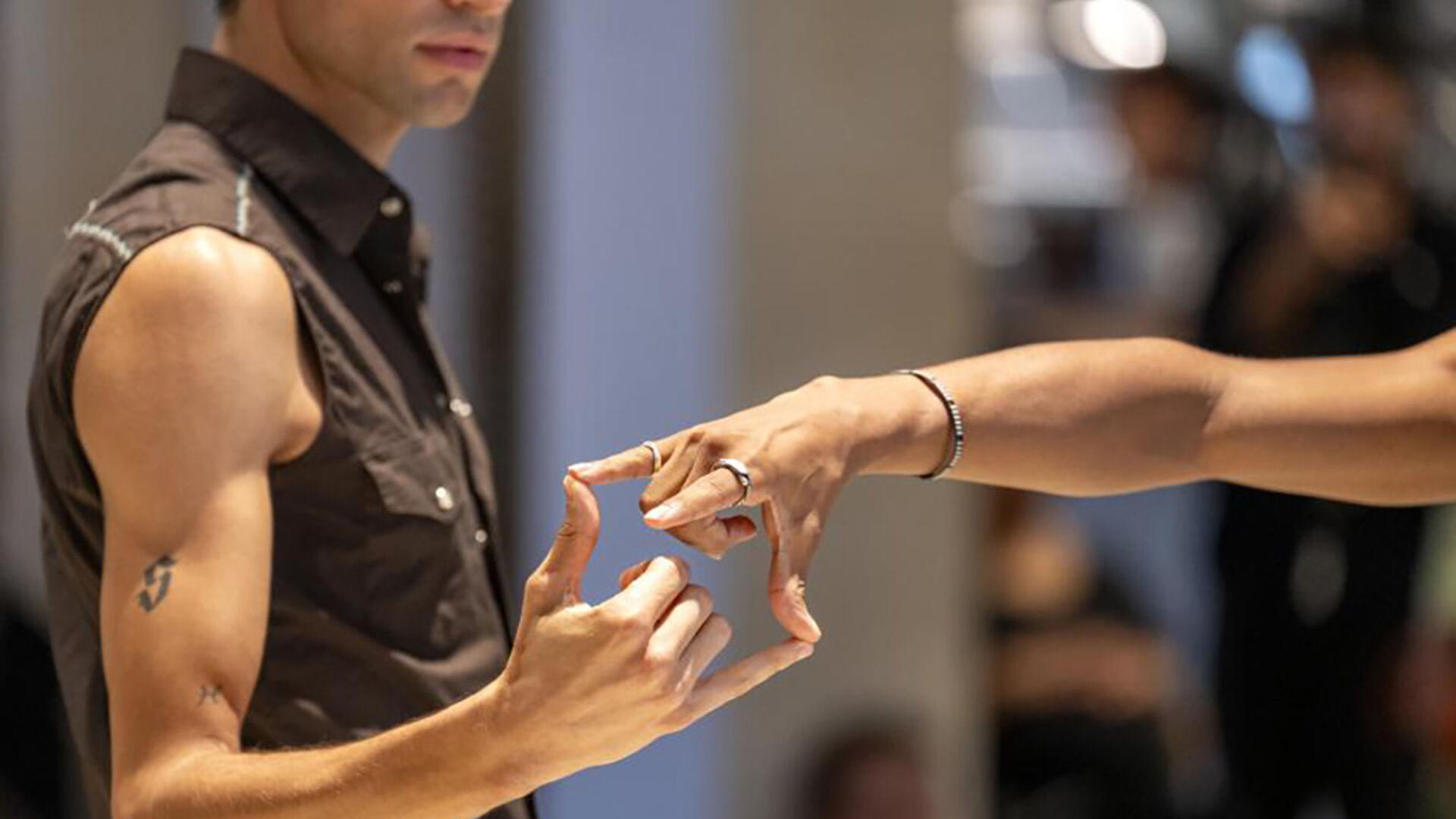Die Fotografie zeigt die Arme zweier Performer:innen, die sich mit den Fingerspitzen von Daumen und kleinem Finger berühren.